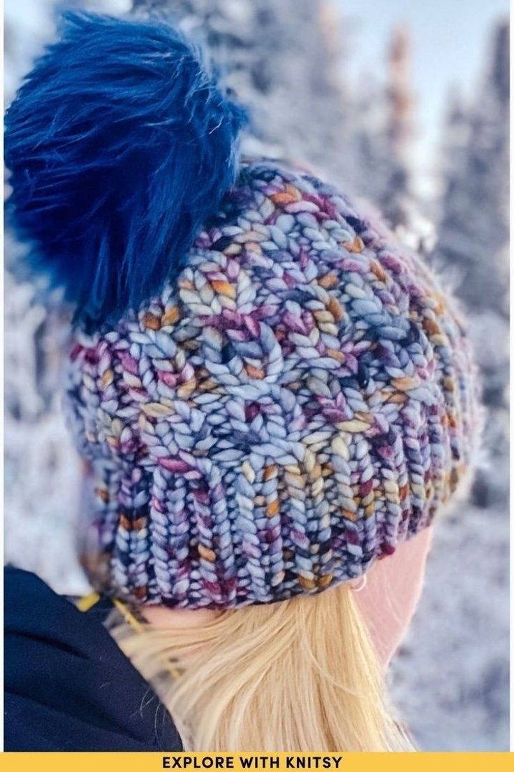 a woman wearing a knitted hat with blue pom - pom on top