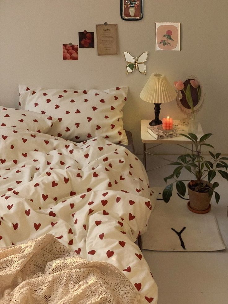 a bed with white sheets and red hearts on it, next to a small table