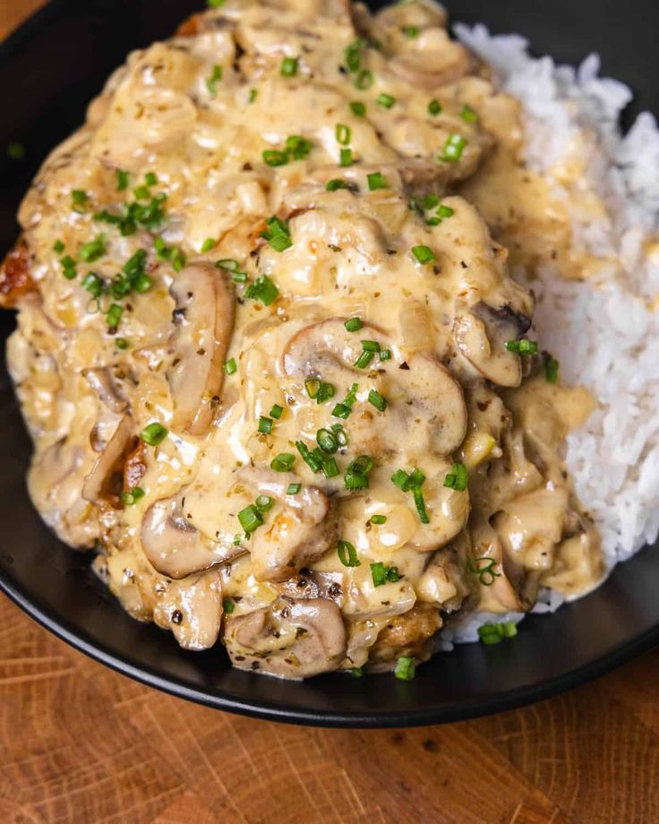 a black plate topped with meat covered in mushroom gravy next to white rice