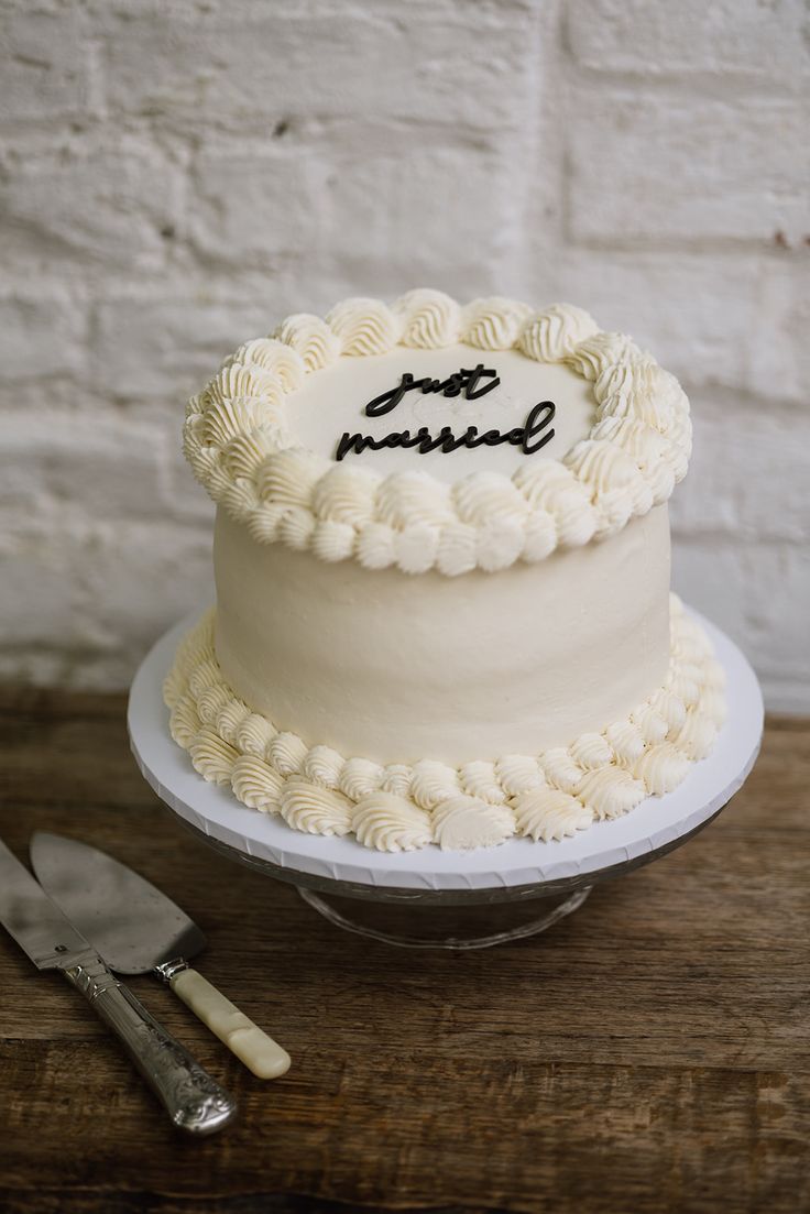 a white cake sitting on top of a wooden table next to a knife and fork