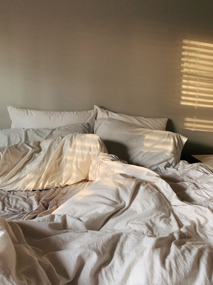 an unmade bed with white sheets and pillows