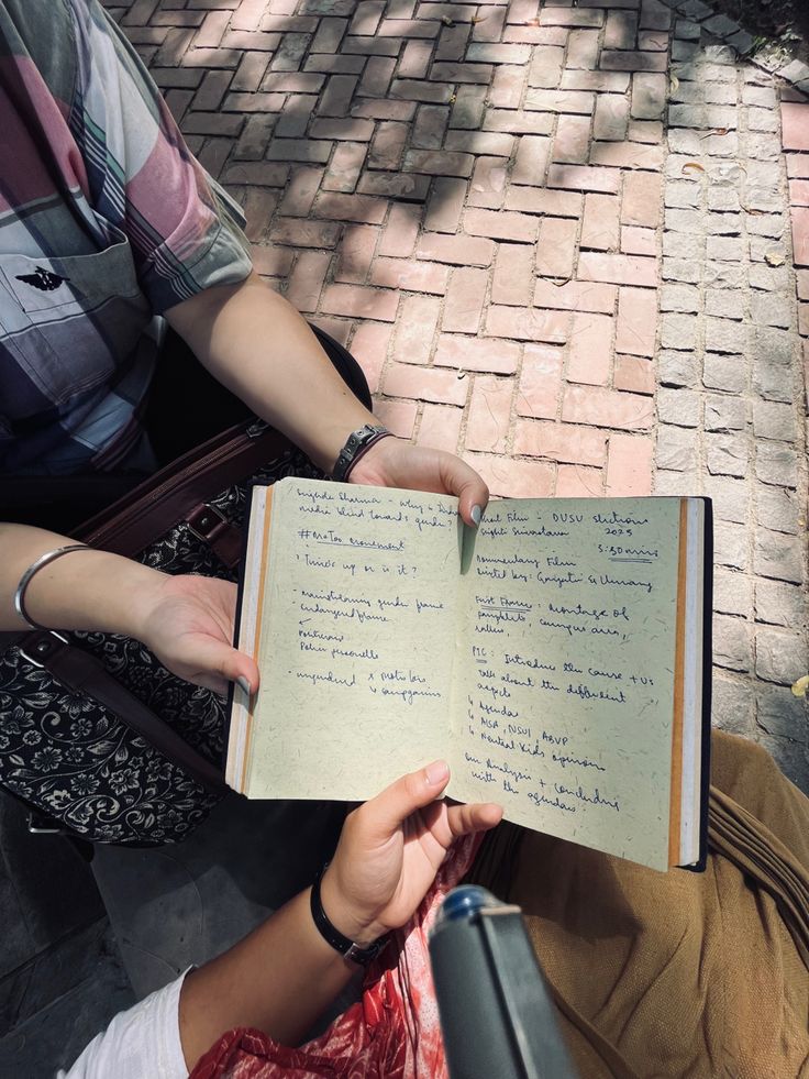 a person sitting on the ground holding an open book with writing on it and another person standing next to them