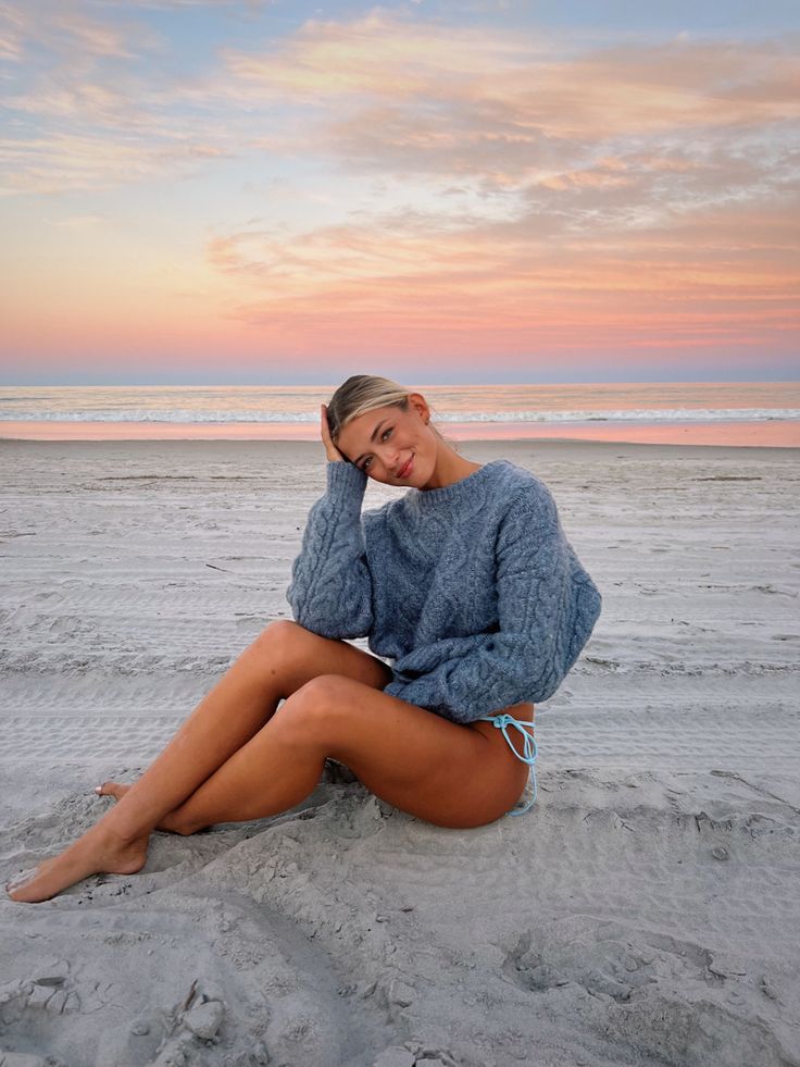 a woman is sitting on the beach at sunset