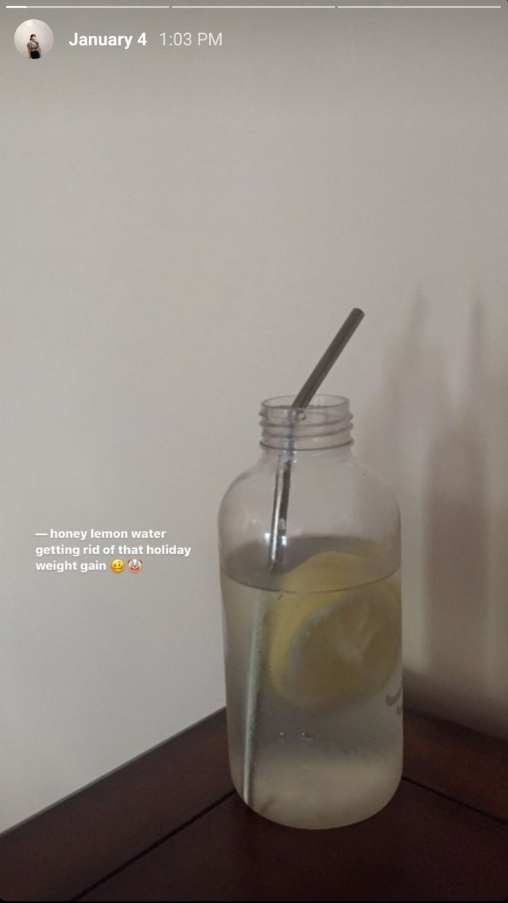 a glass jar filled with water and a lemon on top of a wooden table in front of a white wall