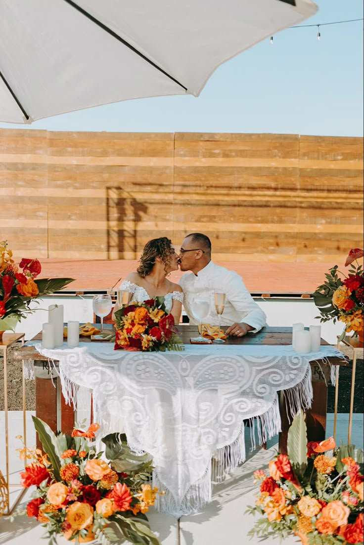 a bride and groom sitting at a table under an umbrella