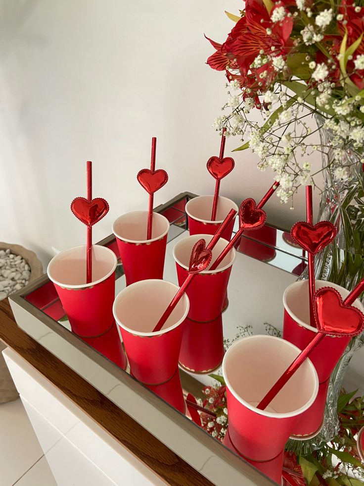 red cups with straws in them are on a tray next to flowers and a vase