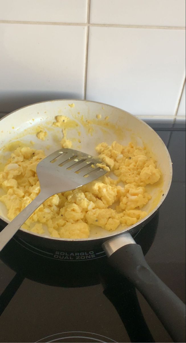 scrambled eggs being cooked in a frying pan with a spatula on the stove