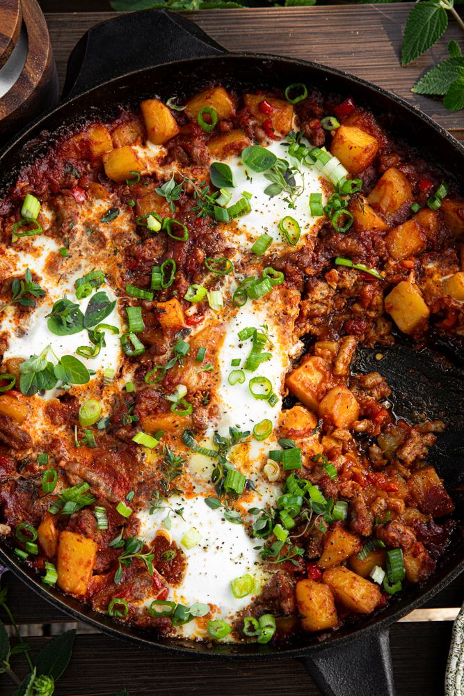 a skillet filled with meat and vegetables on top of a wooden table