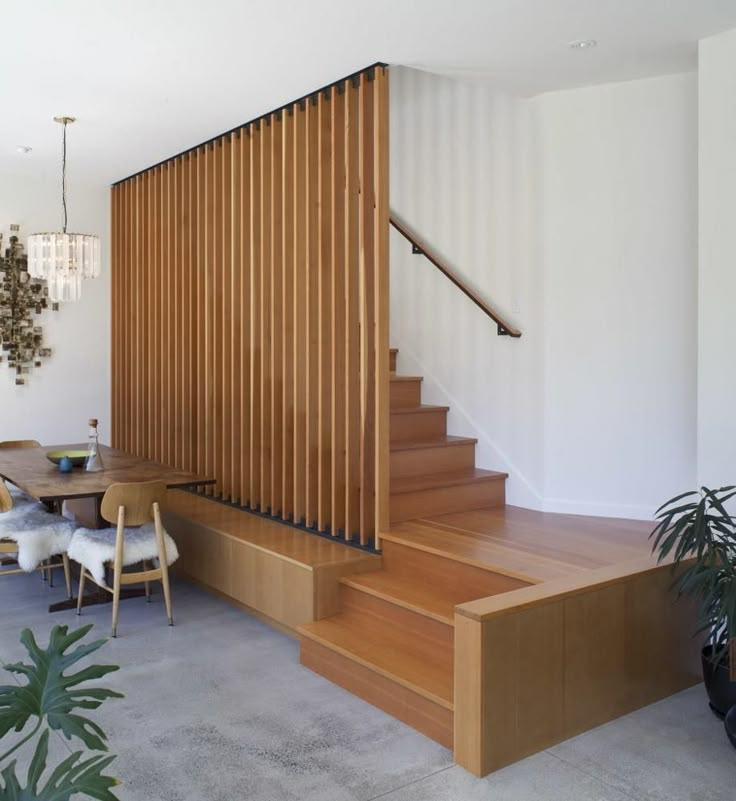 a wooden stair case next to a table and chairs in a room with white walls