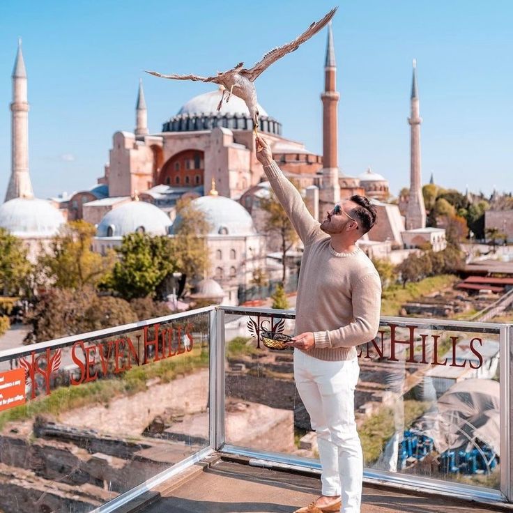 a man standing on top of a balcony next to a bird flying over his head