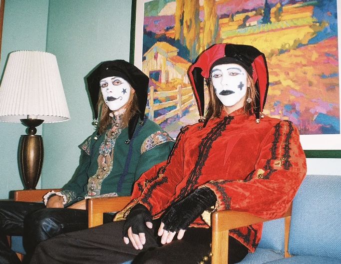 two people with painted faces sitting on chairs in front of a painting and lampshade