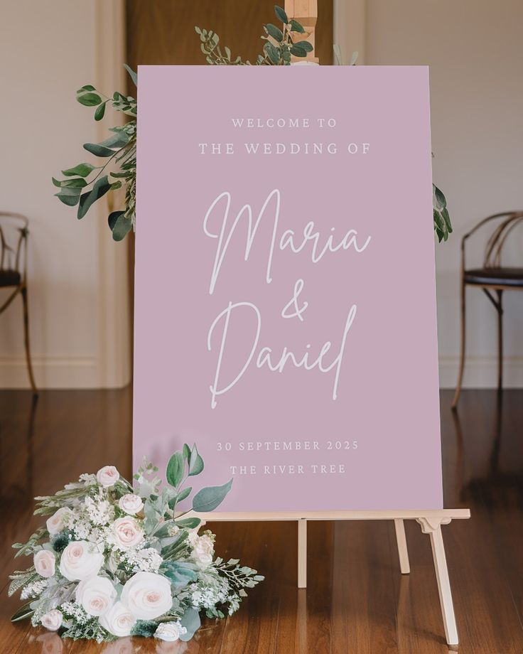 a welcome sign with flowers and greenery sits on the floor next to an easel