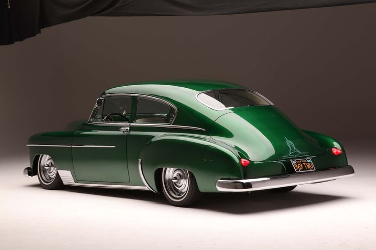 an old green car is parked in front of a black curtain