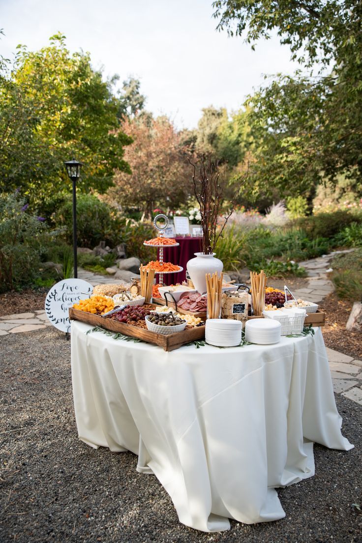 a table topped with food and drinks on top of a gravel road next to trees