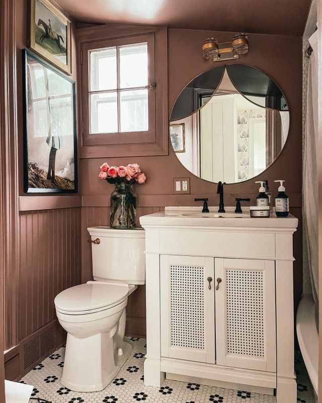 a white toilet sitting next to a sink in a bathroom under a large round mirror