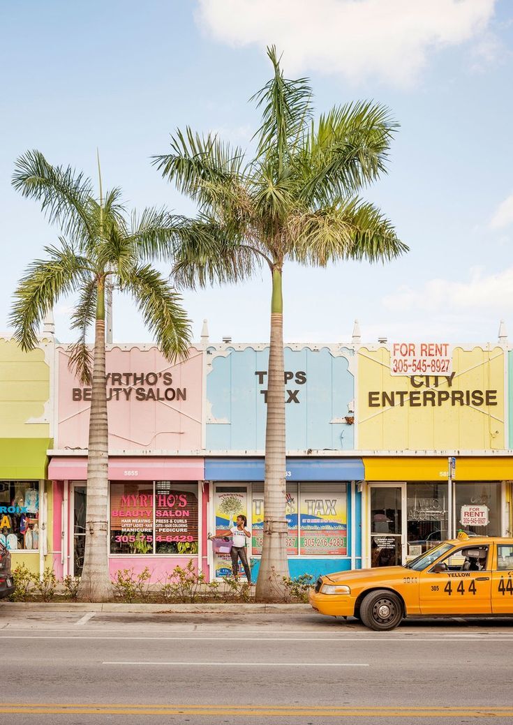 a yellow taxi cab parked in front of a store with palm trees on the street