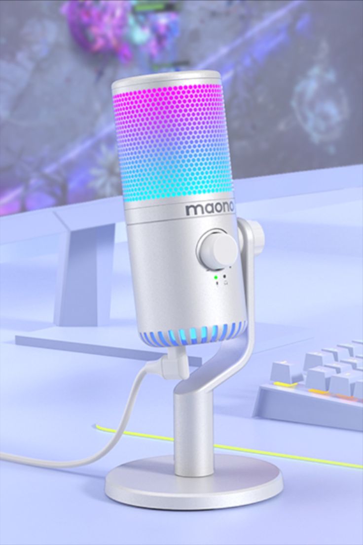 a white microphone on a stand next to a keyboard and computer monitor with colorful lights in the background