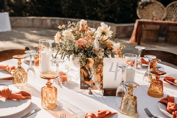 the table is set with wine glasses, candles and flowers in vases on it