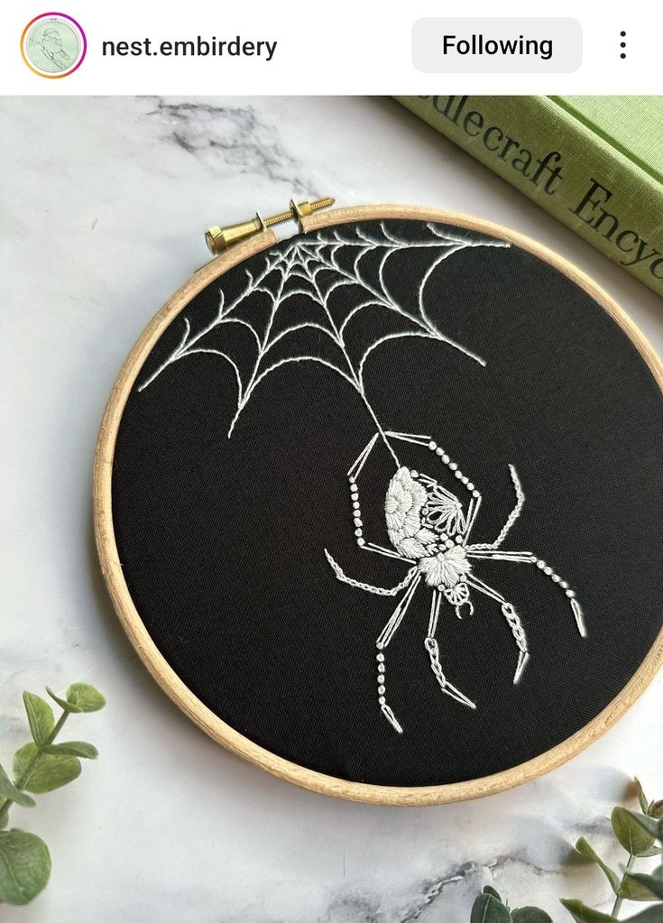 an embroidered spider sits on top of a table next to some green books and a plant