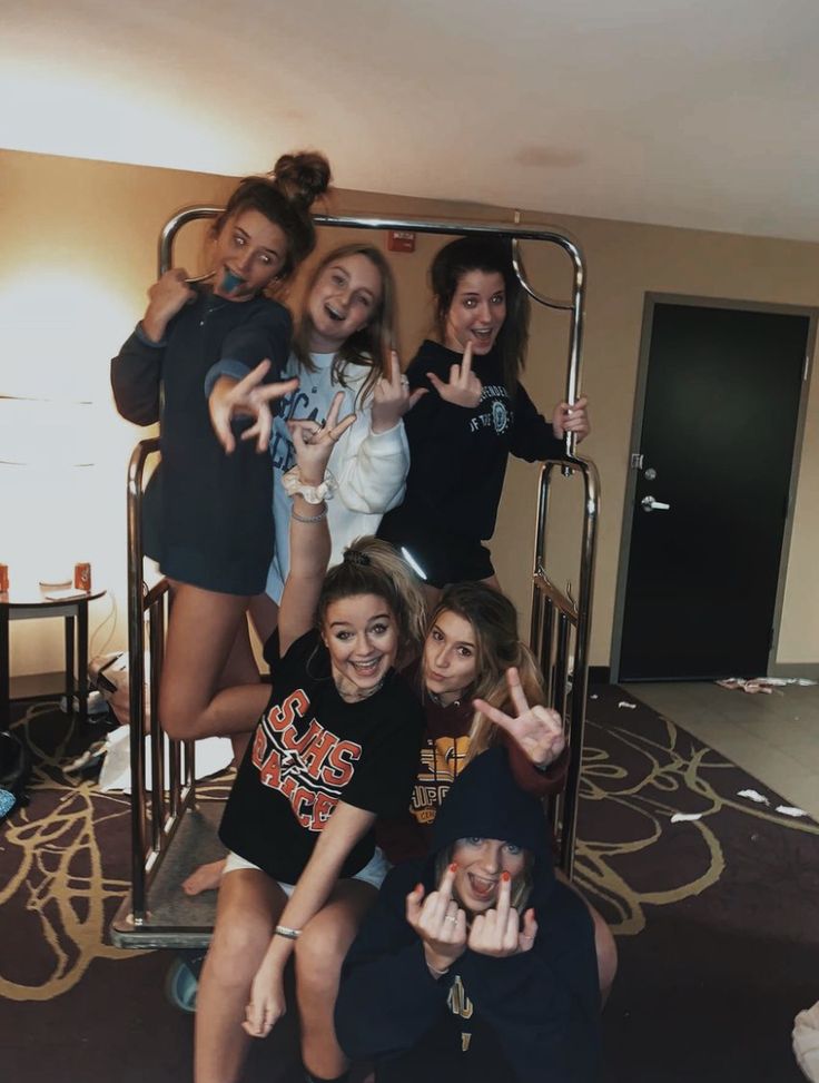 four girls posing for the camera with their hands in the air and one girl pointing at the camera