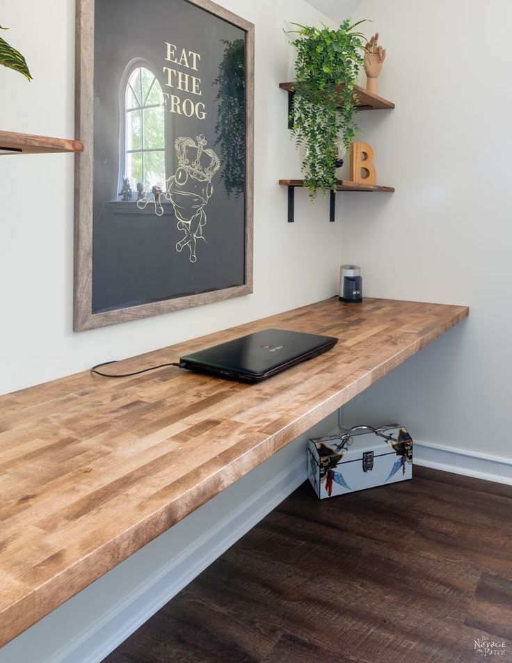 a wooden table with a laptop on it in front of a wall mounted planter