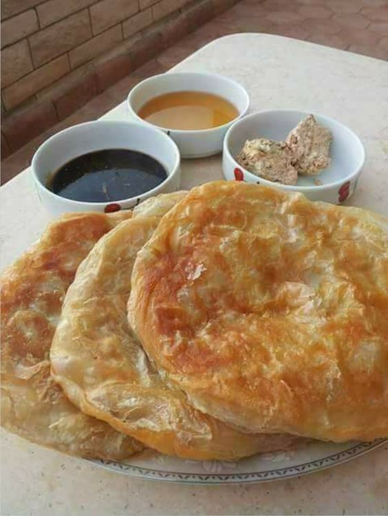 three breads on a plate with dipping sauces next to them and two small bowls