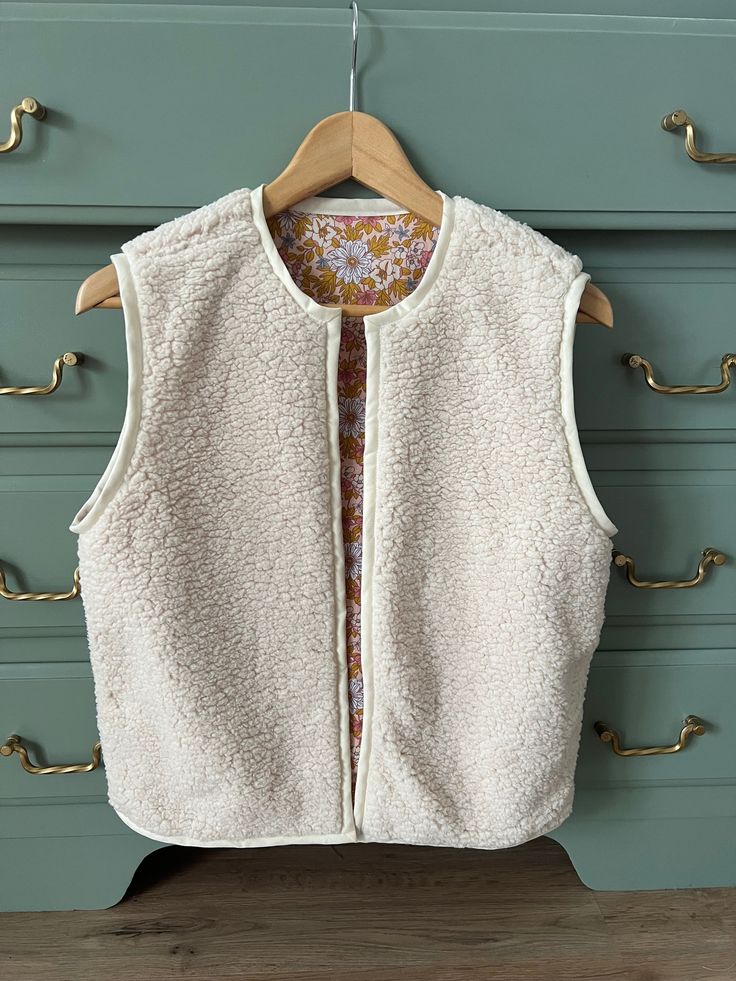 a white vest hanging on a wooden hanger in front of a blue dresser with gold handles