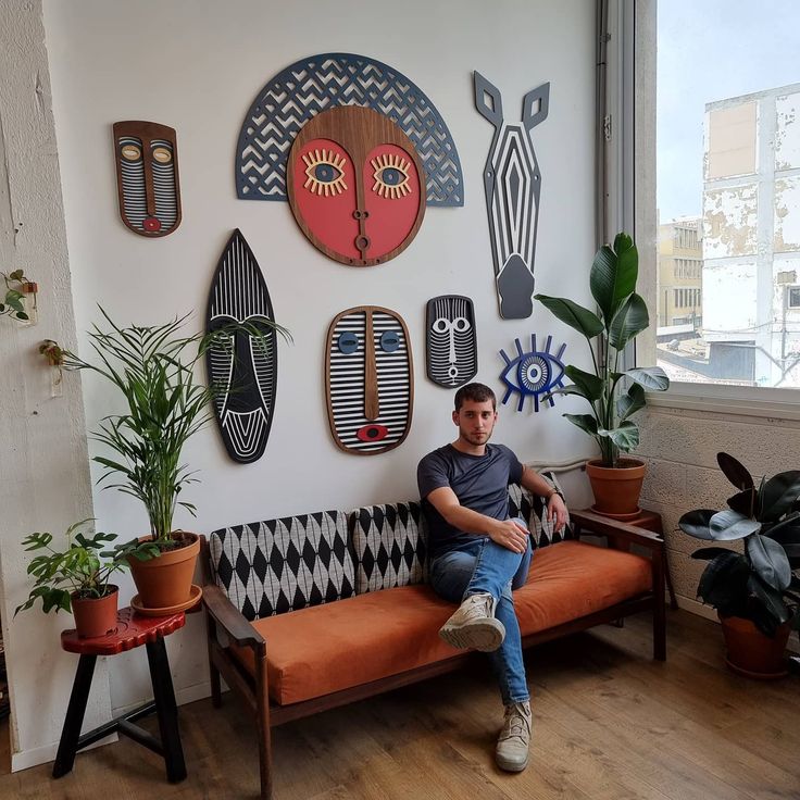 a man sitting on top of a couch in front of a wall covered with art