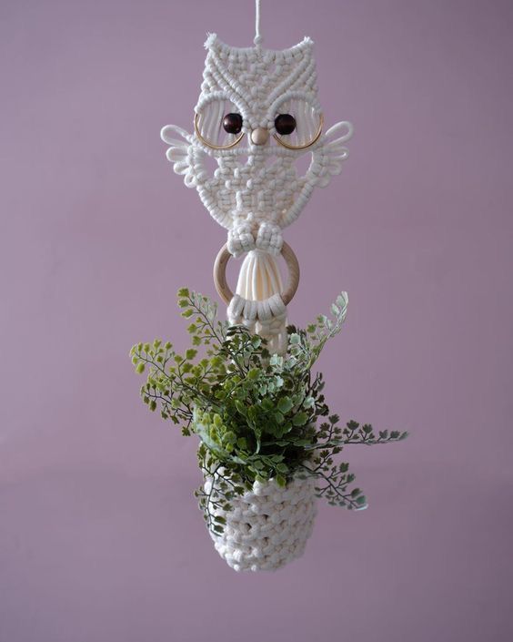 a white vase filled with plants and an owl hanging from it's side on a purple wall