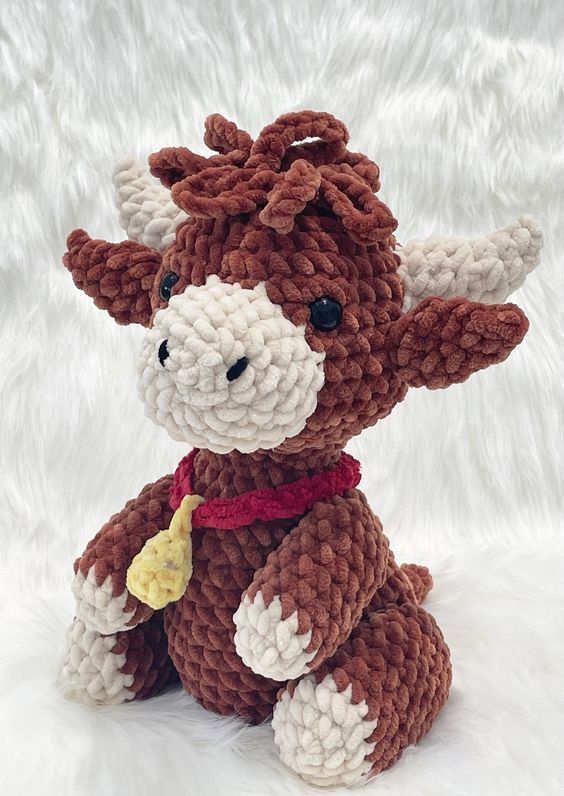 a brown and white knitted cow sitting on top of a white fur covered floor