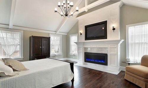 a bedroom with white walls and wood floors, a fireplace in the corner, two windows on either side