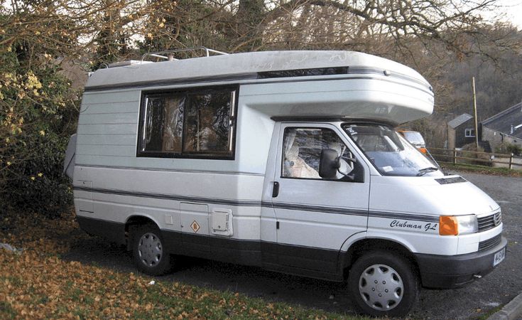 an rv is parked on the side of the road in front of some trees and bushes