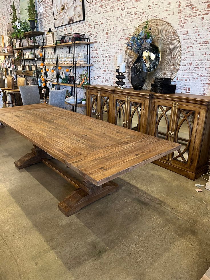 a large wooden table sitting in front of a wall with shelves and chairs behind it