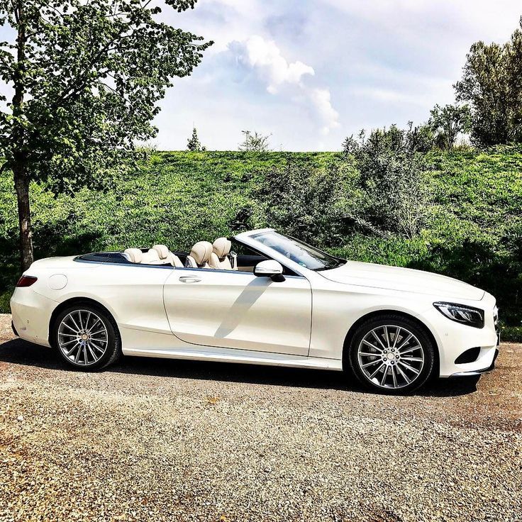 a white convertible car parked on the side of a road with trees in the background