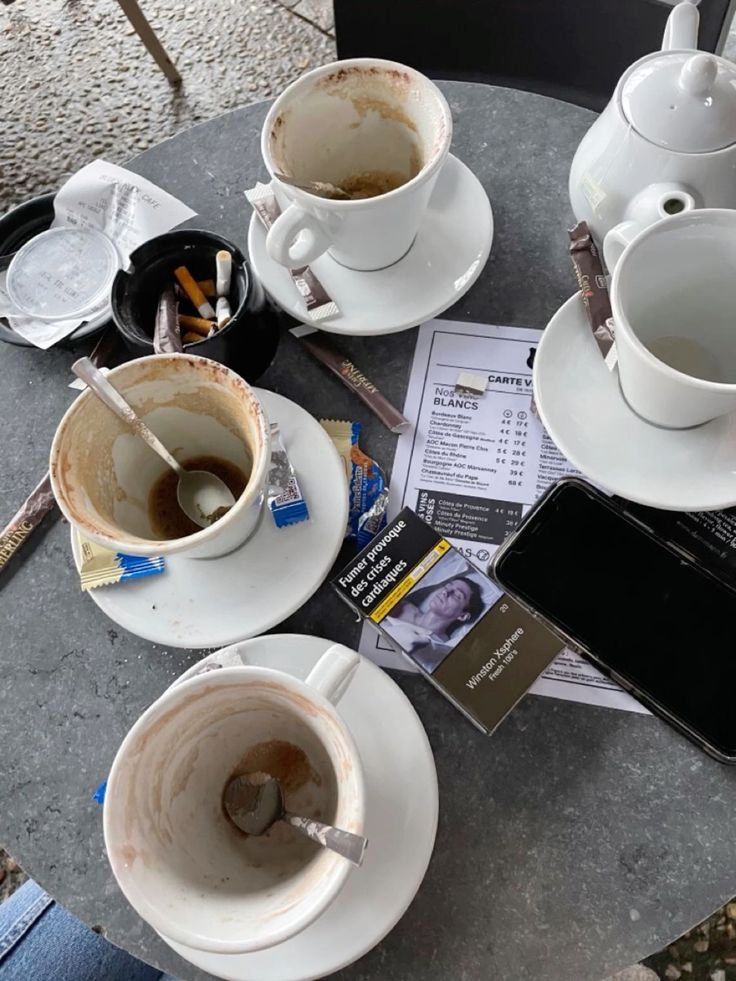 two cups and saucers sitting on top of a table next to a cell phone