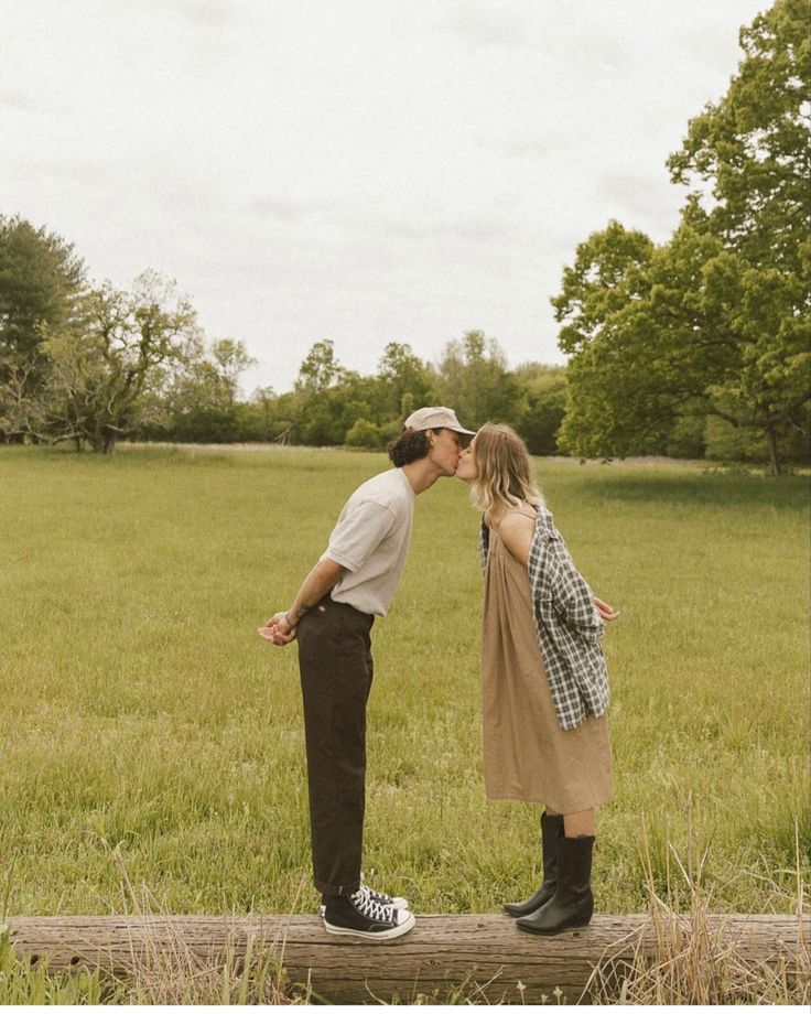 a man and woman kissing in the middle of a field on a wooden plank with trees in the background