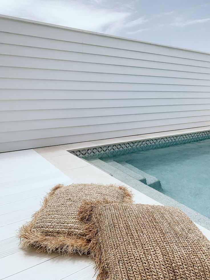 a burlap pillow sitting next to an empty swimming pool with a white house in the background