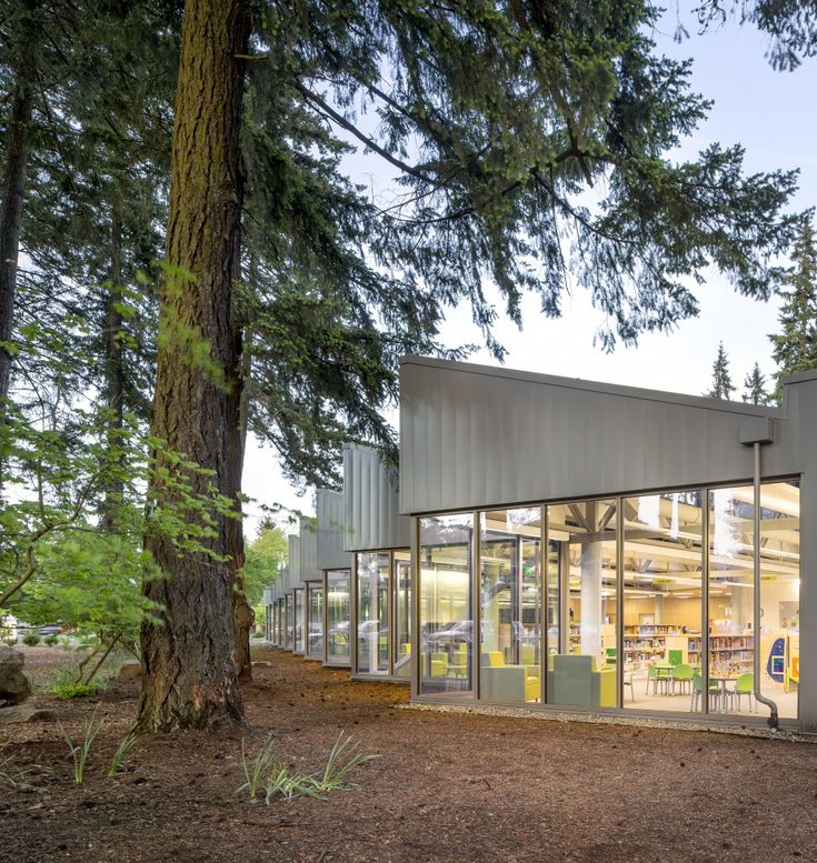 the building is surrounded by trees and has glass walls on both sides that allow for people to sit outside