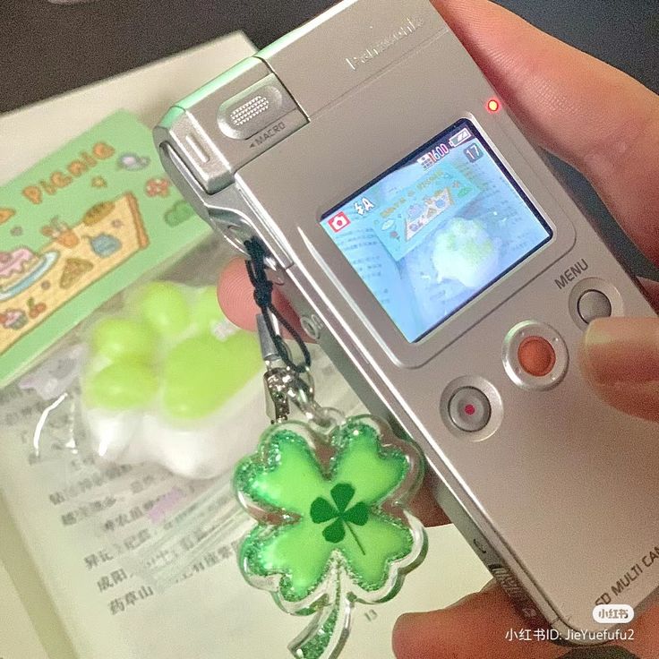 a person holding a cell phone with a shamrock keychain attached to the back