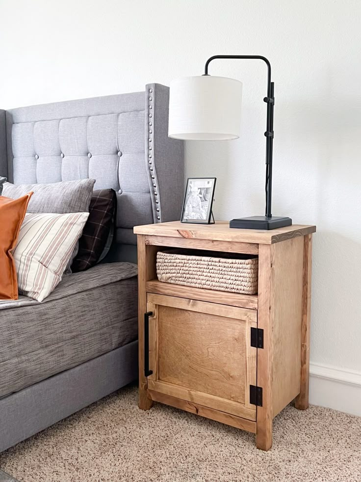 a bed with a gray headboard and wooden night stand next to a grey couch