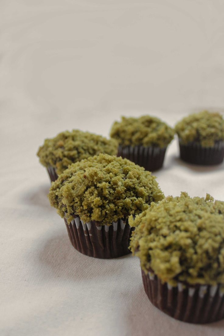 four chocolate cupcakes with green crumbs sitting on a white table cloth