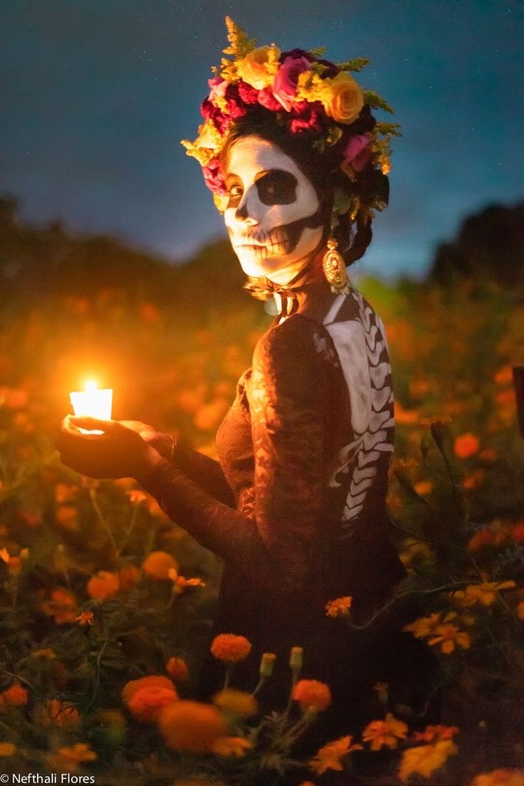 a woman in skeleton makeup holding a lit candle with flowers on her head and face