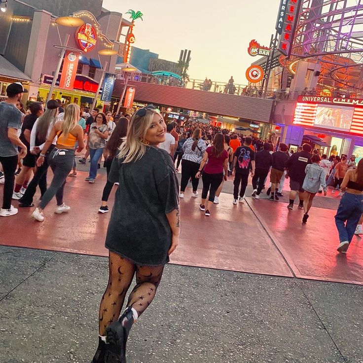 a woman standing in the middle of a crowded street with lots of people walking around