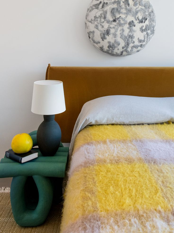 a bed with a yellow blanket next to a lamp and a painting on the wall