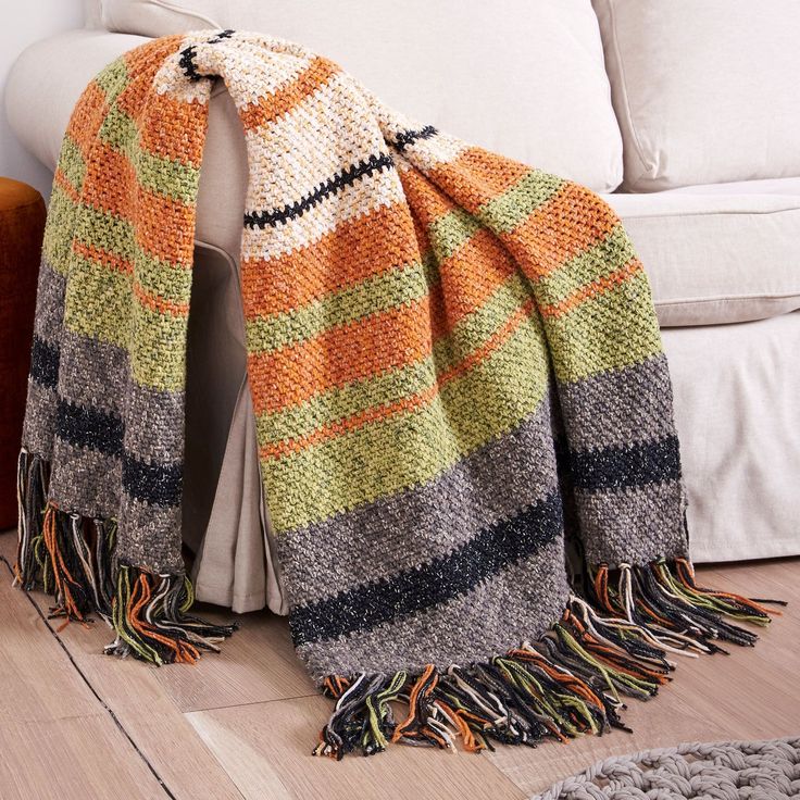 an orange, green and black blanket sitting on top of a wooden floor next to a white couch