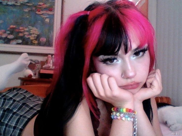 a woman with pink hair and bracelets on her wrist posing for the camera in front of a bed