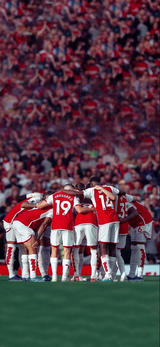 a group of soccer players huddle together on the field in front of an audience