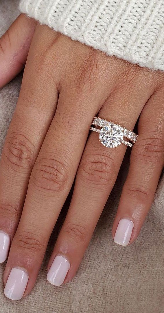 a woman's hand with two engagement rings on her fingers and the other hand holding an engagement ring