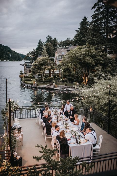 a group of people sitting around a table on top of a patio next to the water