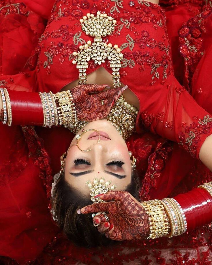 a woman in red and gold is laying down with her hands on her face while wearing an elaborate head piece